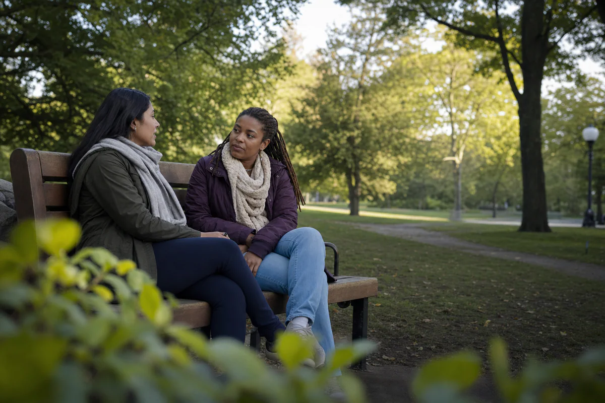 Two friends talking on a quiet park bench with attentive, unforced body language.