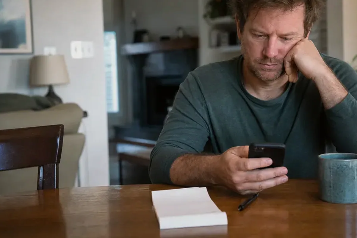 A person at a sunlit desk placing a phone face down and opening a notebook to one simple task.