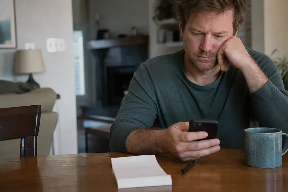 A person at a sunlit desk placing a phone face down and opening a notebook to one simple task.