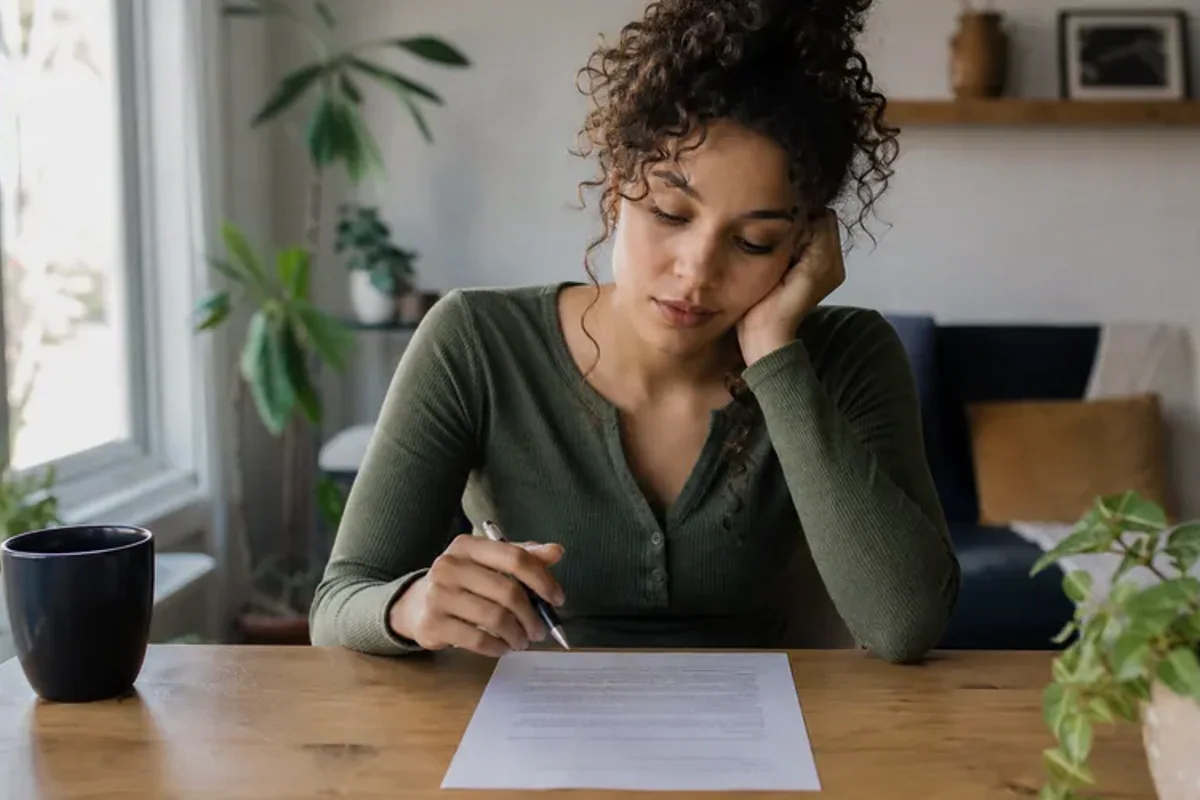 A person at a sunlit desk placing a phone face down and opening a notebook to one simple task.