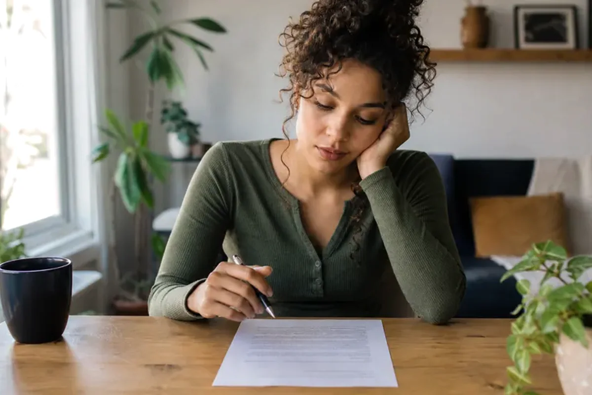 A person at a sunlit desk placing a phone face down and opening a notebook to one simple task.