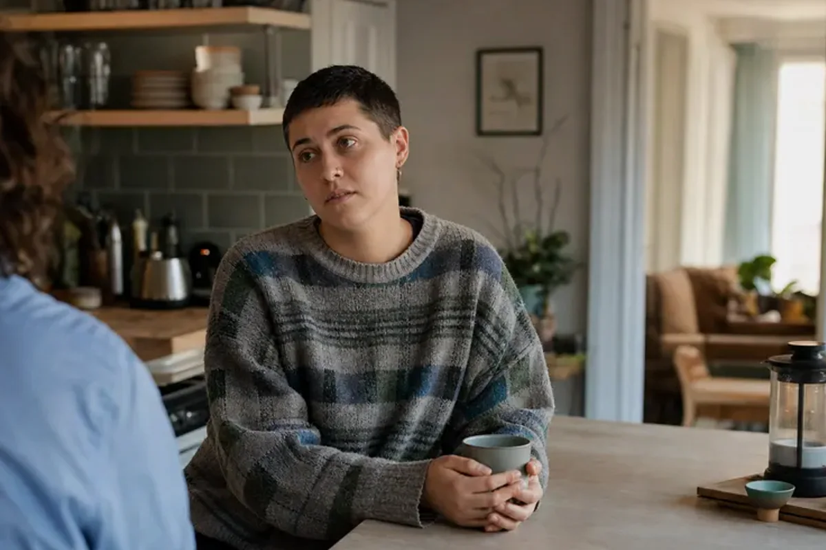 A person standing by a bright window, resting one hand lightly near the chest and noticing a slow breath.