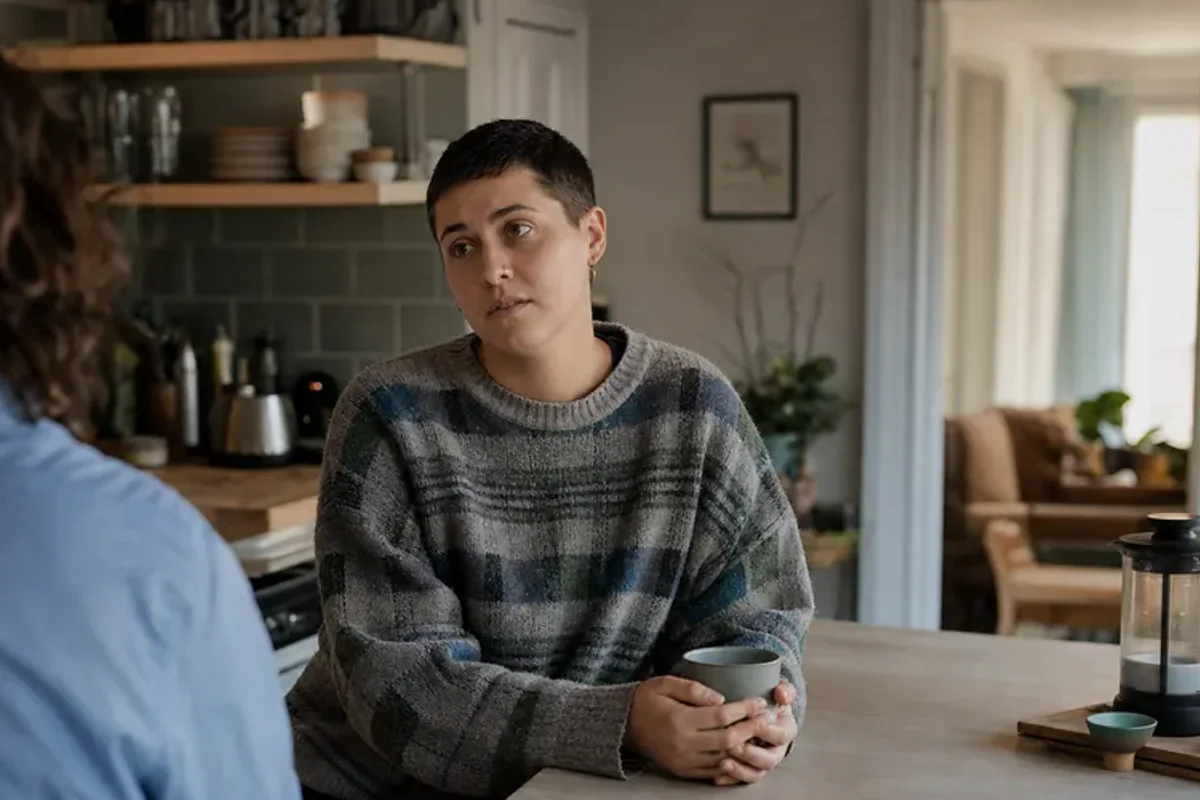 A person standing by a bright window, resting one hand lightly near the chest and noticing a slow breath.