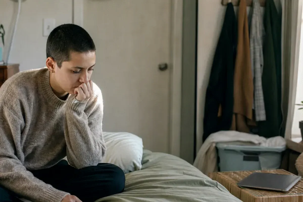 A person standing by a bright window, resting one hand lightly near the chest and noticing a slow breath.