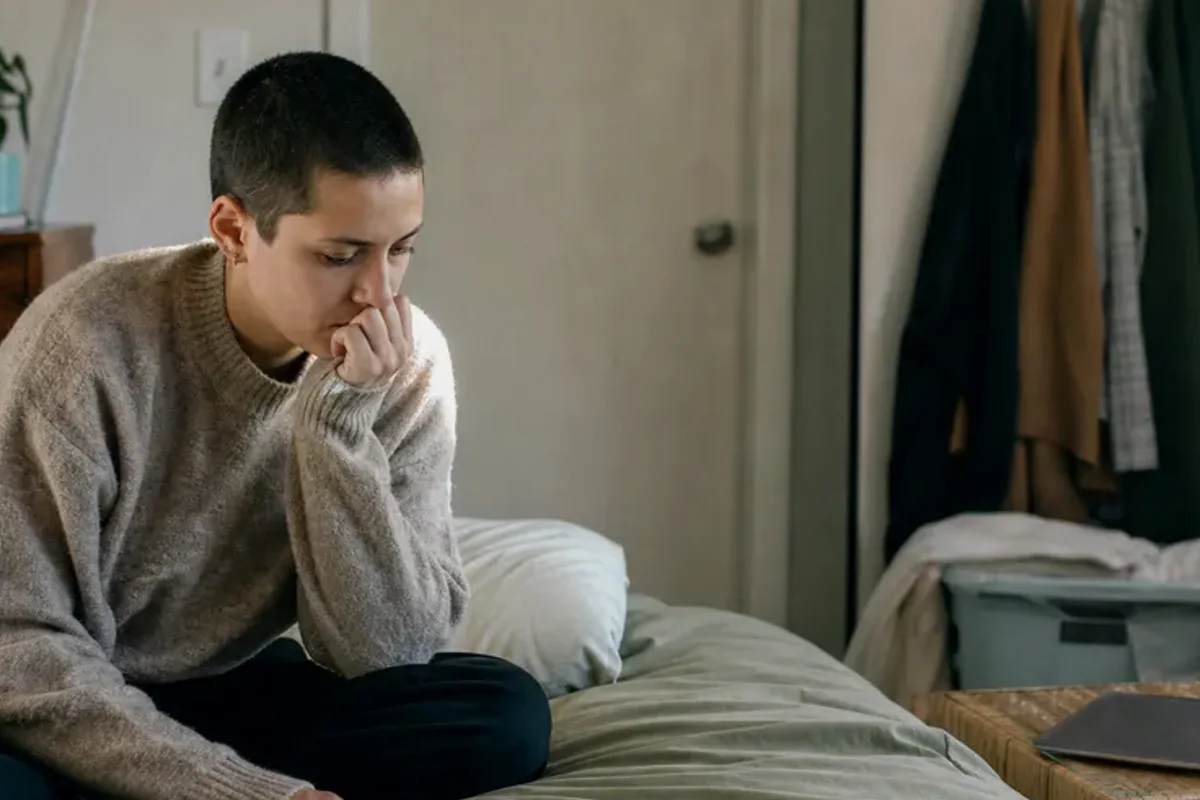 A person standing by a bright window, resting one hand lightly near the chest and noticing a slow breath.