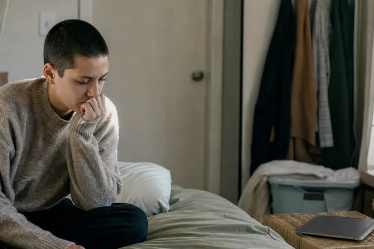 A person standing by a bright window, resting one hand lightly near the chest and noticing a slow breath.