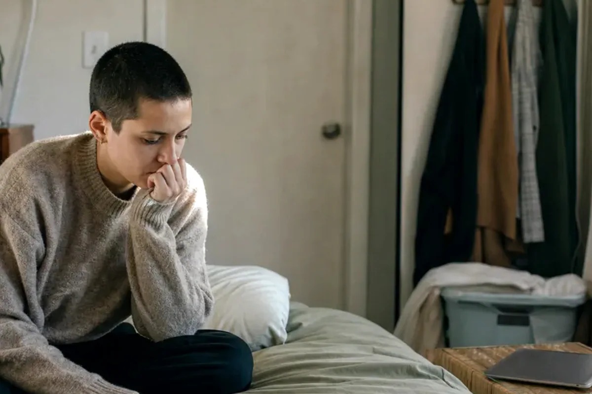 A person standing by a bright window, resting one hand lightly near the chest and noticing a slow breath.