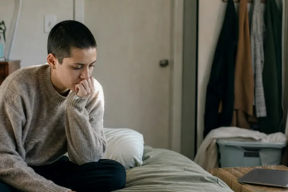 A person standing by a bright window, resting one hand lightly near the chest and noticing a slow breath.
