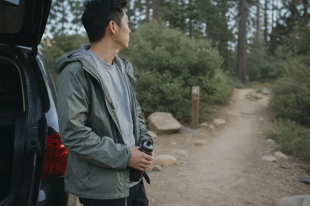 A person stepping from a softly lit doorway onto a quiet tree-lined path.