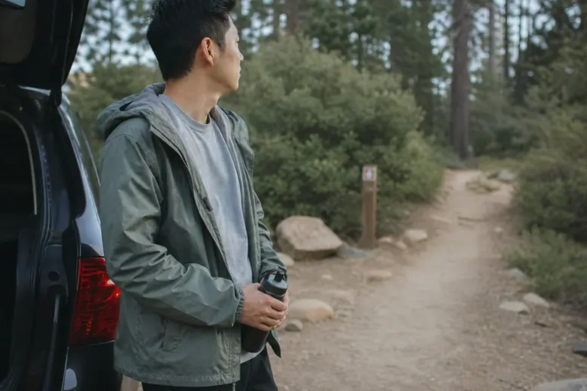 A person stepping from a softly lit doorway onto a quiet tree-lined path.