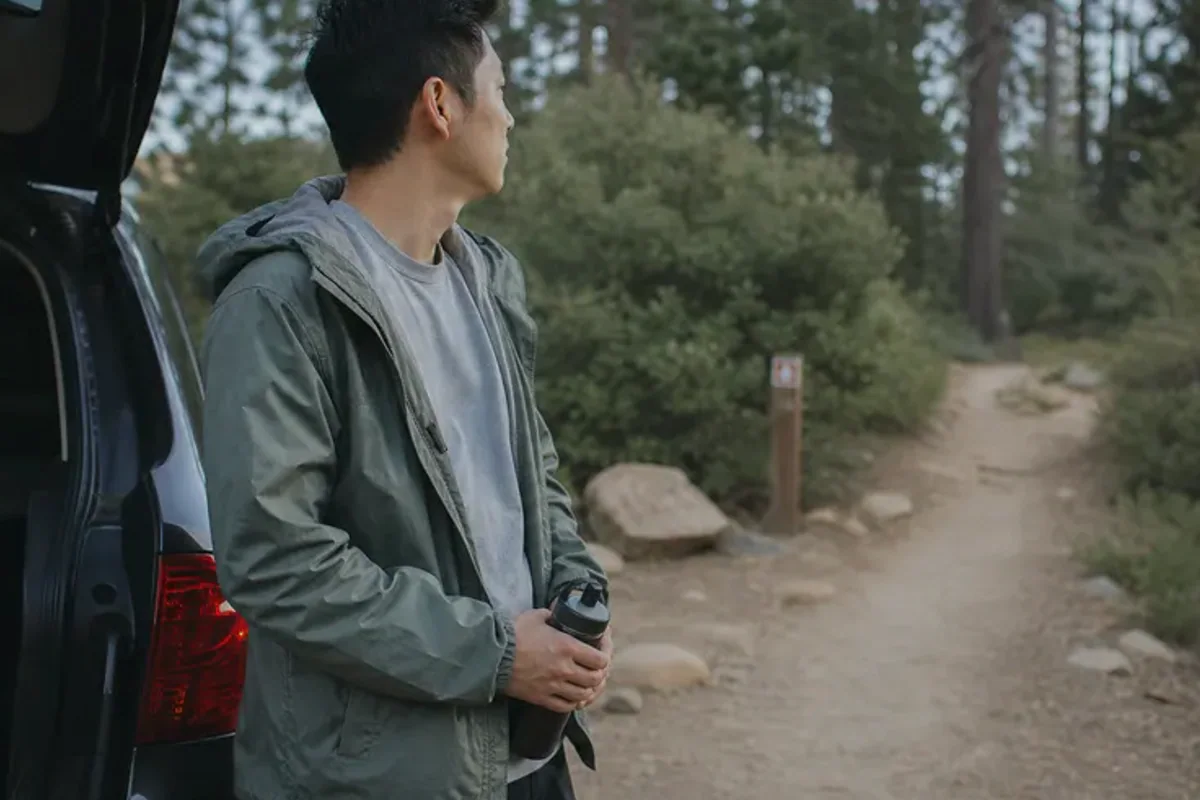 A person stepping from a softly lit doorway onto a quiet tree-lined path.