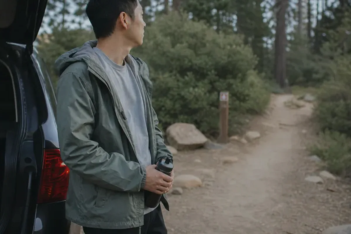 A person stepping from a softly lit doorway onto a quiet tree-lined path.