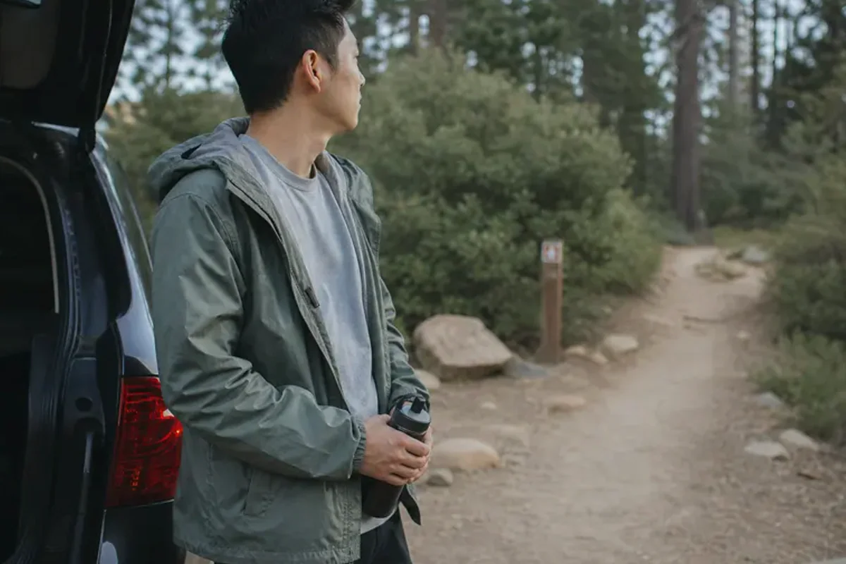 A person stepping from a softly lit doorway onto a quiet tree-lined path.
