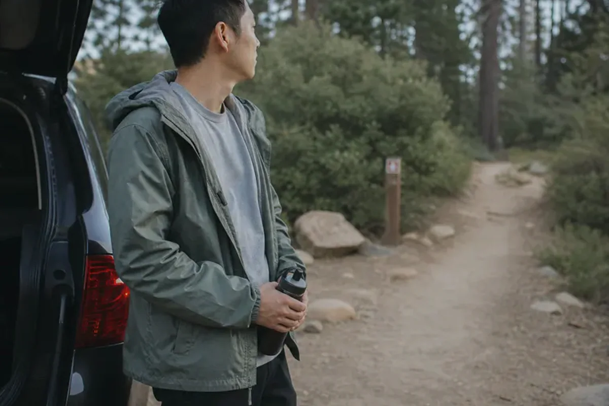 A person stepping from a softly lit doorway onto a quiet tree-lined path.