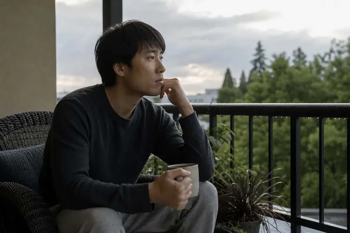 A person standing by a bright window, resting one hand lightly near the chest and noticing a slow breath.
