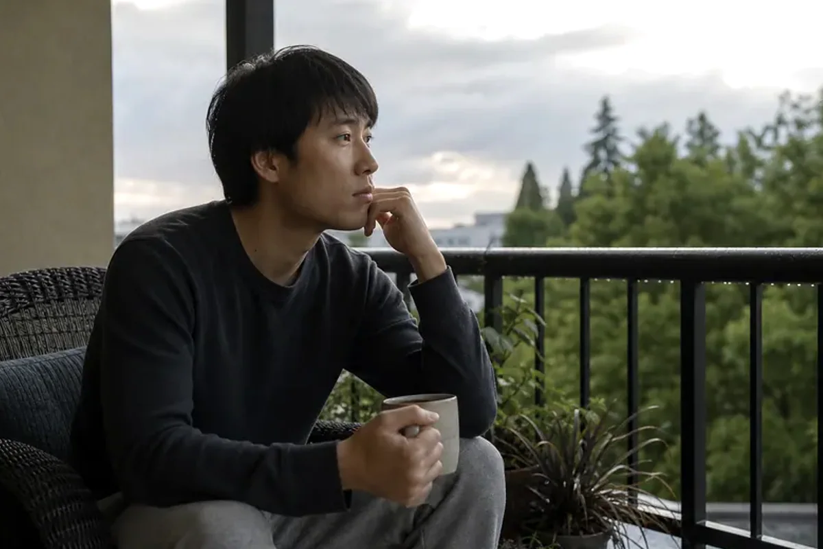 A person standing by a bright window, resting one hand lightly near the chest and noticing a slow breath.