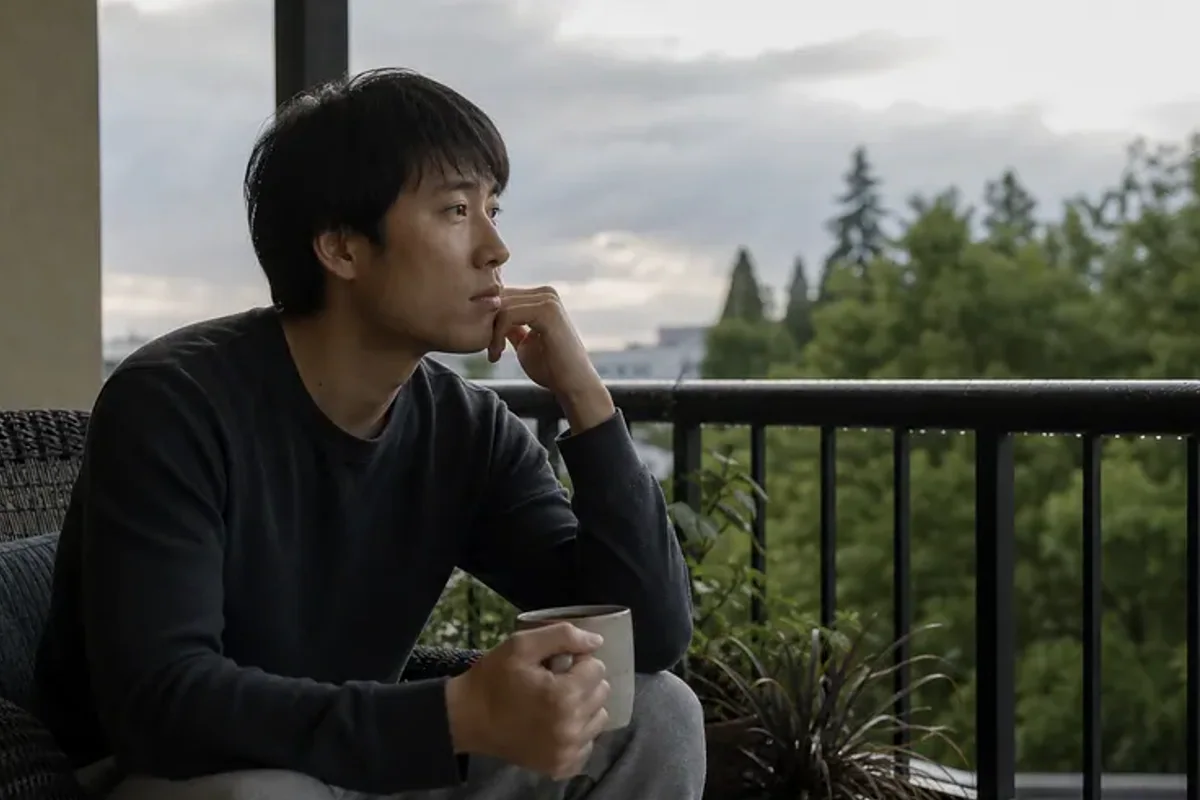 A person standing by a bright window, resting one hand lightly near the chest and noticing a slow breath.