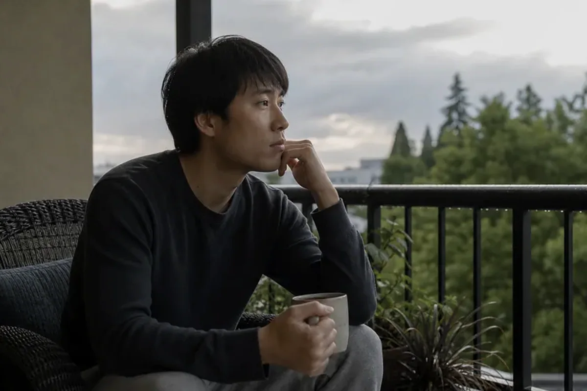 A person standing by a bright window, resting one hand lightly near the chest and noticing a slow breath.