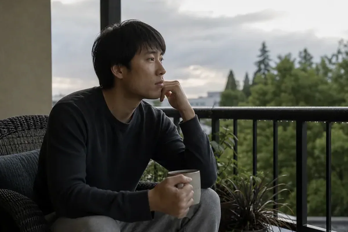 A person standing by a bright window, resting one hand lightly near the chest and noticing a slow breath.