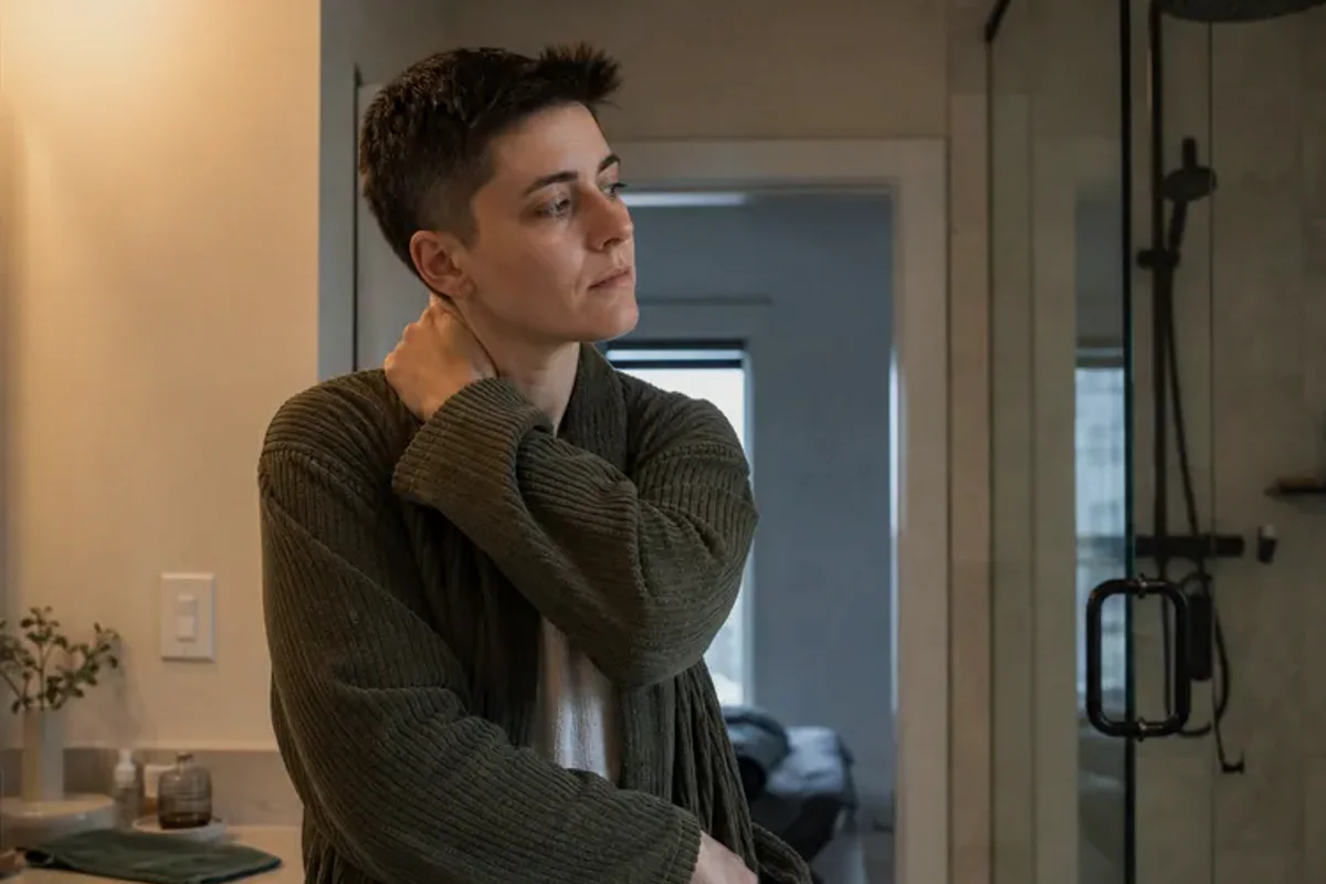 A person standing by a bright window, resting one hand lightly near the chest and noticing a slow breath.