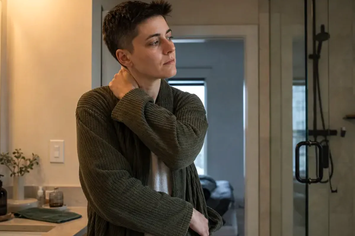 A person standing by a bright window, resting one hand lightly near the chest and noticing a slow breath.
